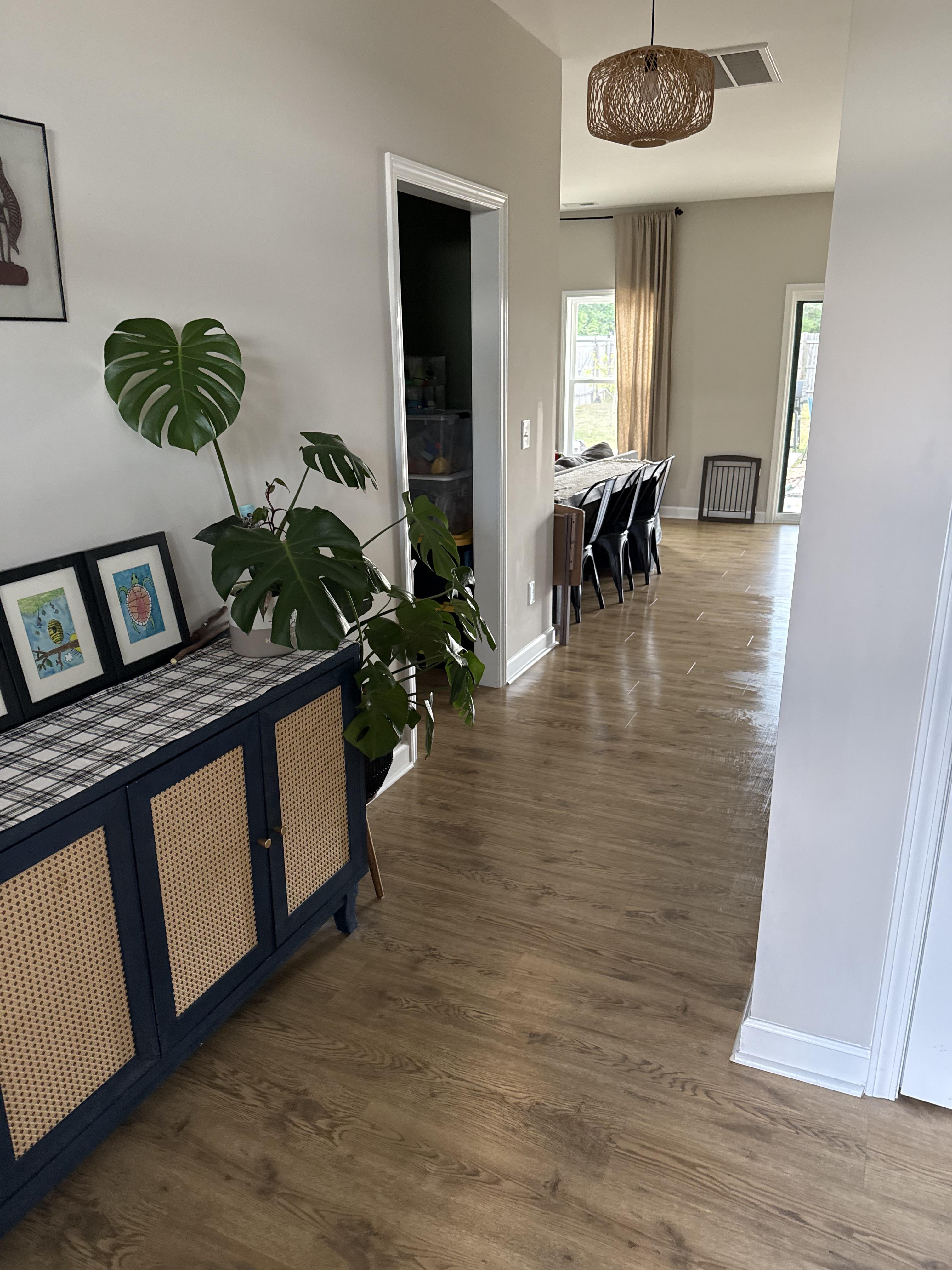 Interior view of a residential hallway featuring light wood flooring and white walls leading into a dining area.